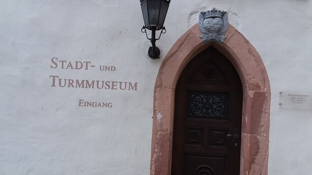 Entrada de un edificio con un letrero que dice "Stadt- und Turmuseum Eingang" y un escudo decorativo sobre la puerta.