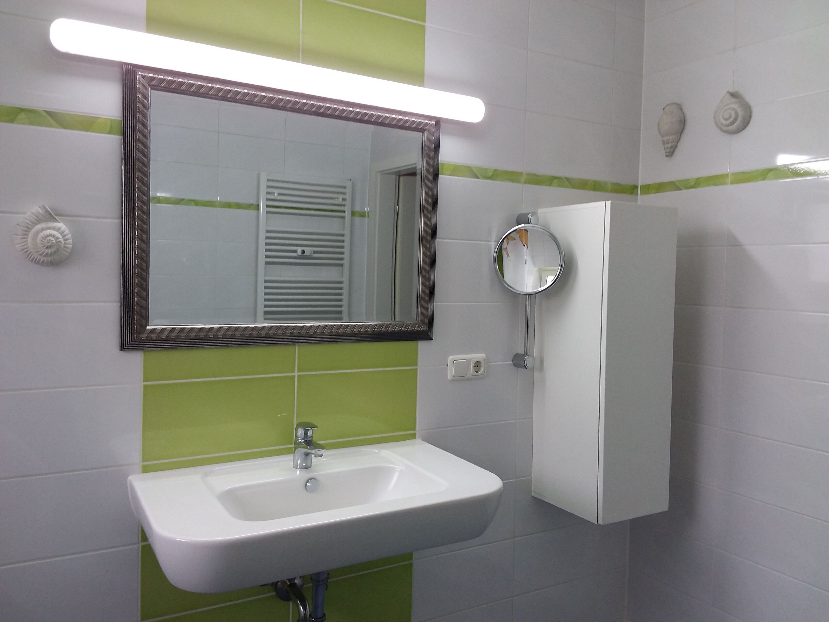 Un baño con un lavabo blanco, un espejo y azulejos verde a rayas.