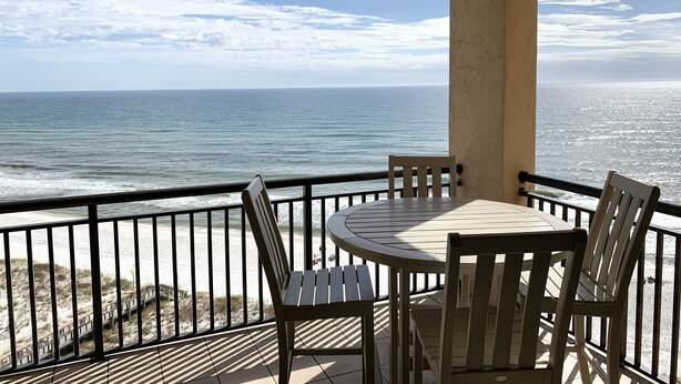 Un balcon avec une table ronde et des chaises, donnant sur une plage et l’océan.