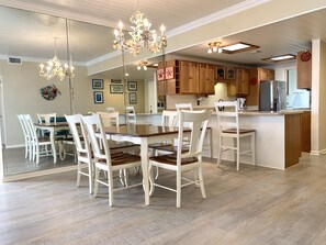 Un vaste espace dédié à la salle à manger, avec une table en bois et des chaises blanches, une cuisine dotée de meubles en bois et un lustre.