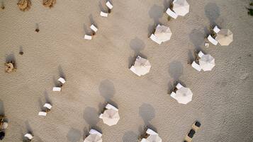 Vista aérea de una playa con múltiples sombrillas blancas y sillas de playa dispuestas en un patrón cuadriculado.