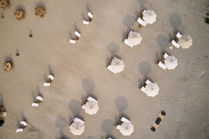 Vista aérea de una playa con múltiples sombrillas blancas y sillas de playa dispuestas en un patrón cuadriculado.