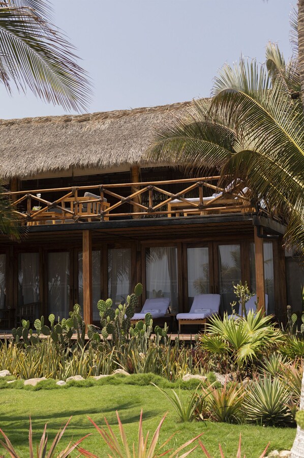 Un resort con estructura de techo de paja, terraza de madera y exuberante jardín tropical.