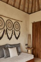 Una habitación con una cama, una pared con tres atrapasueños, una puerta de madera y una mesita con un libro.