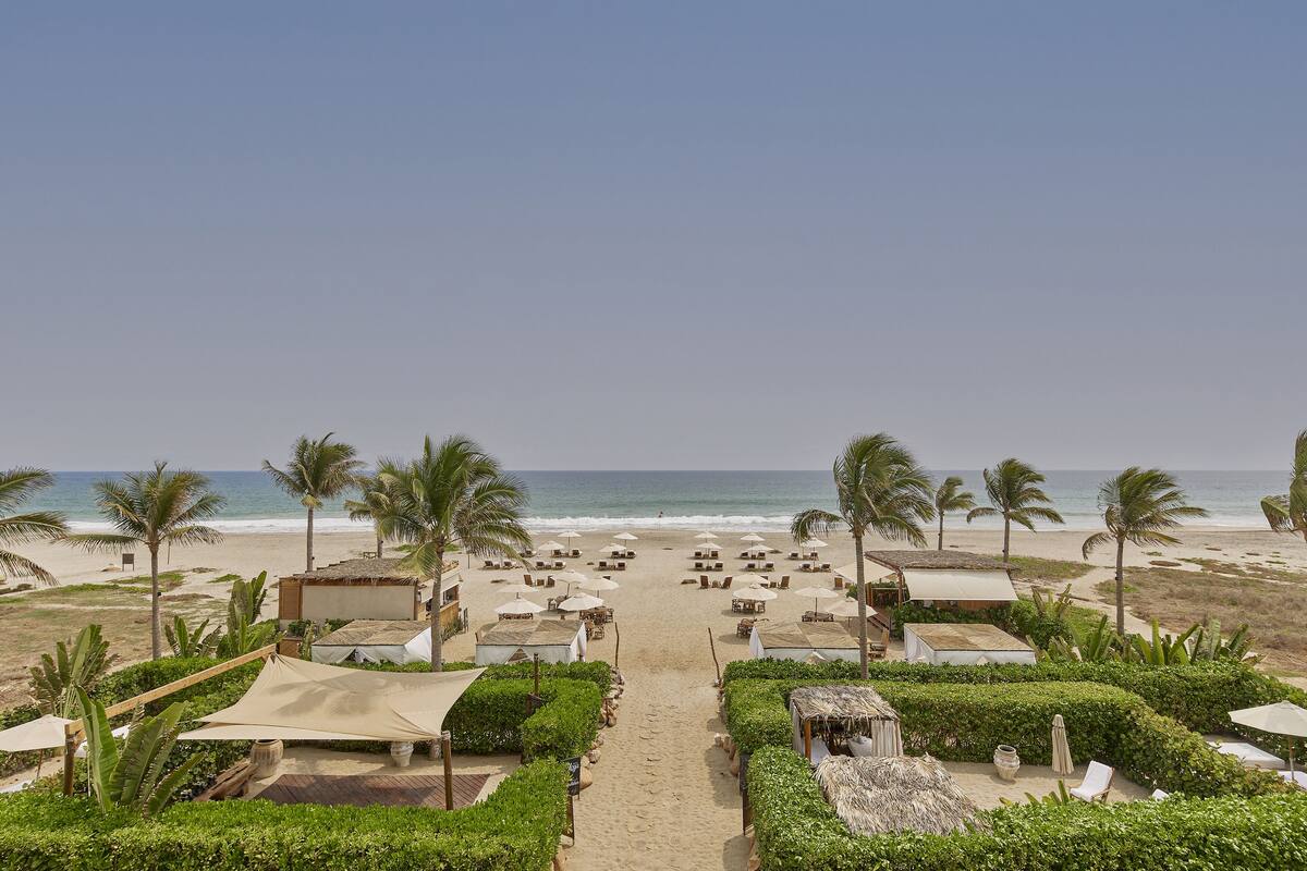 Un complexe hôtelier de bord de mer avec un chemin dégagé menant à l’océan, entouré de palmiers et de chaises de plage.