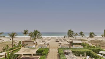 A beach resort with a clear pathway leading to the ocean, surrounded by palm trees and beach chairs.