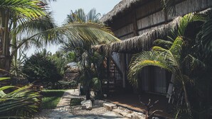 Un jardin tropical avec un bâtiment à toit de chaume, un sentier en pierre et des palmiers.