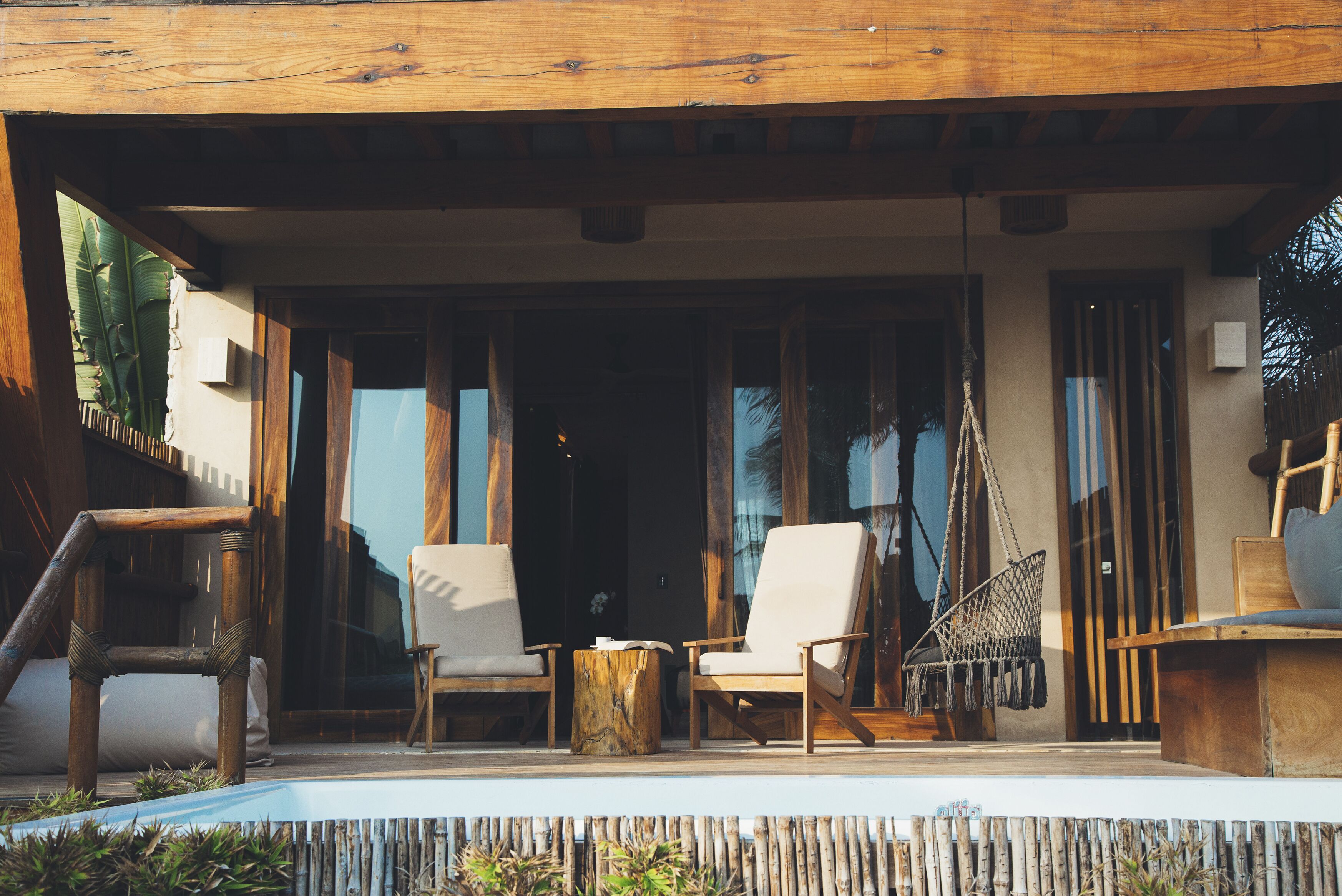 Un espacio al aire libre con dos sillones blancos acolchados, una mesa de madera y un sillón colgante.