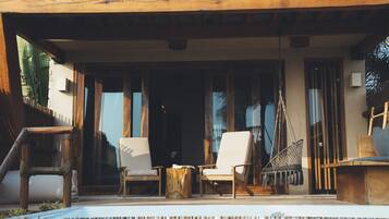 Un espacio al aire libre con dos sillones blancos acolchados, una mesa de madera y un sillón colgante.