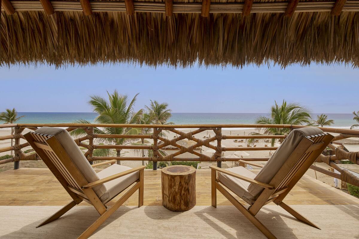 Un salon de plage avec deux chaises longues en bois et une petite table ronde, donnant sur l’océan.