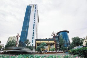 A tall building with a modern design, a fountain in the foreground, and a parking area with cars. - Jinlong Yufeng Hotel (Changde Huanlecheng High Speed Railway Station) (Changde)