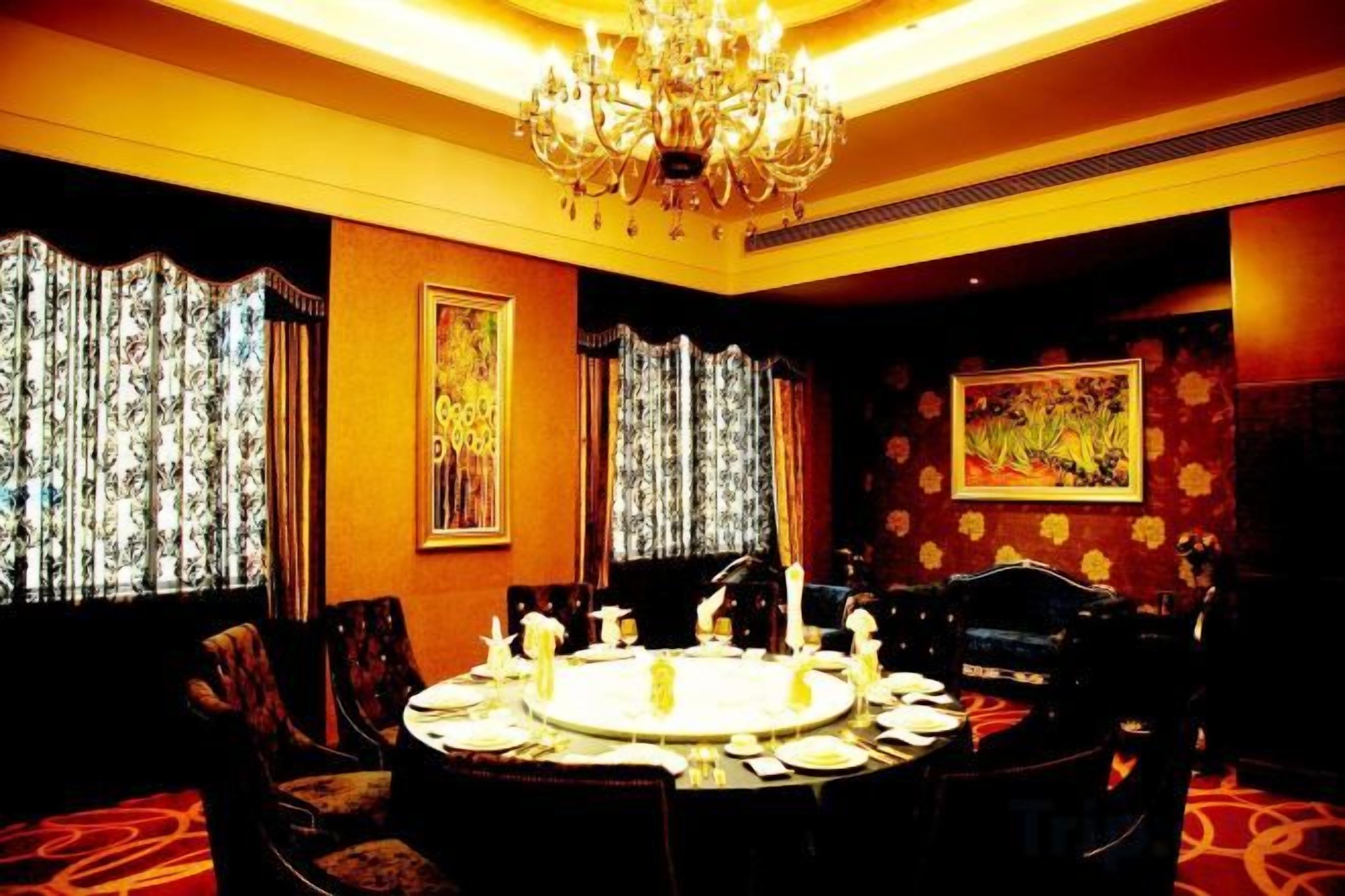 A dining room with a round table set for four, surrounded by chairs, with a chandelier above and curtains on the windows.