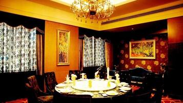 A dining room with a round table set for four, surrounded by chairs, with a chandelier above and curtains on the windows.