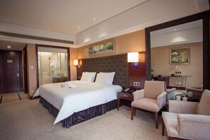A hotel room with a large bed, two bedside tables, a chair, a desk, and a painting on the wall. - Jinlong Yufeng Hotel (Changde Huanlecheng High Speed Railway Station) (Changde)