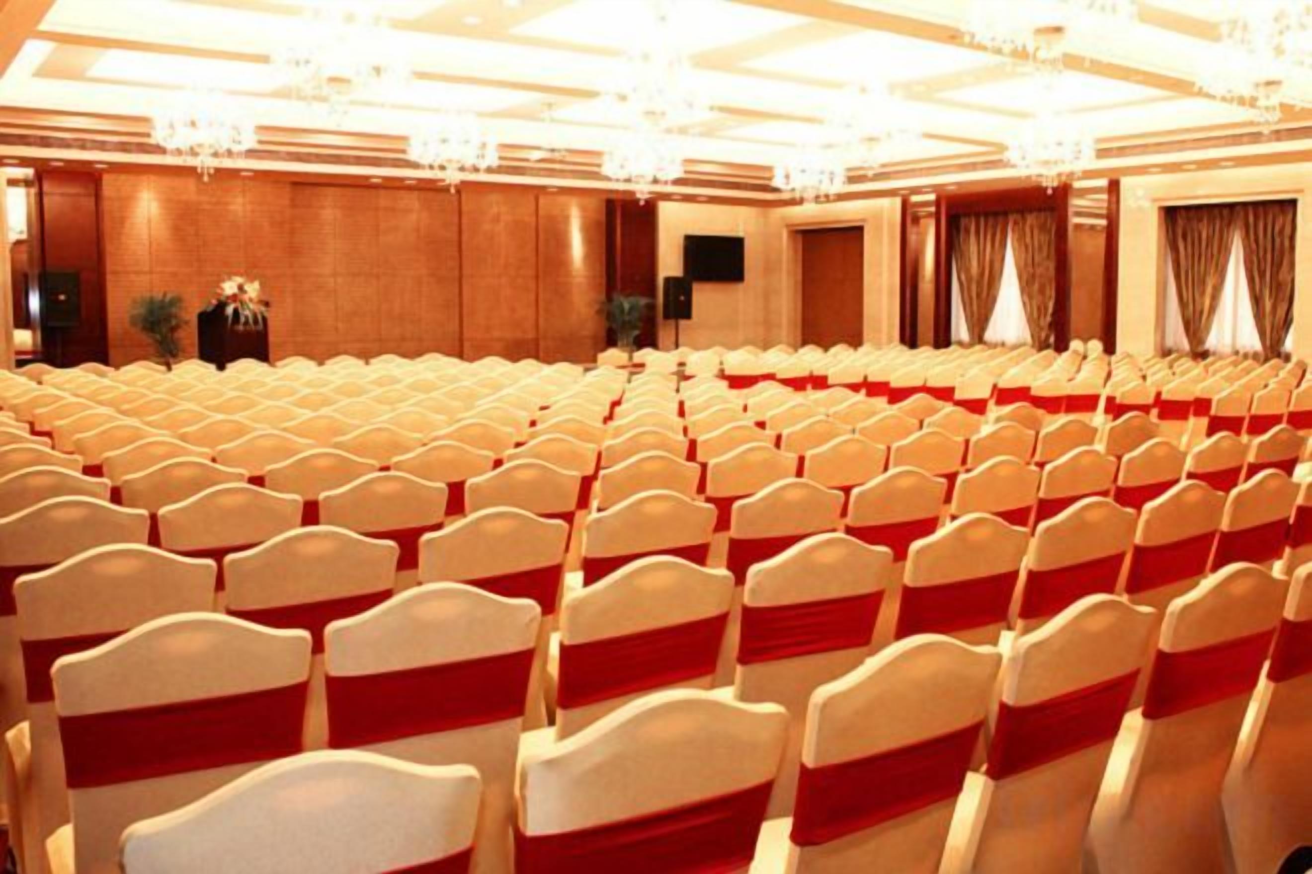 A conference room with rows of chairs, a stage, and a chandelier.