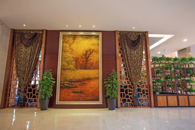 A lobby with a large painting, potted plants, and a decorative partition.