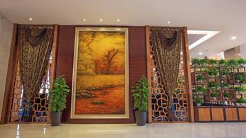 A lobby with a large painting, potted plants, and a decorative partition.