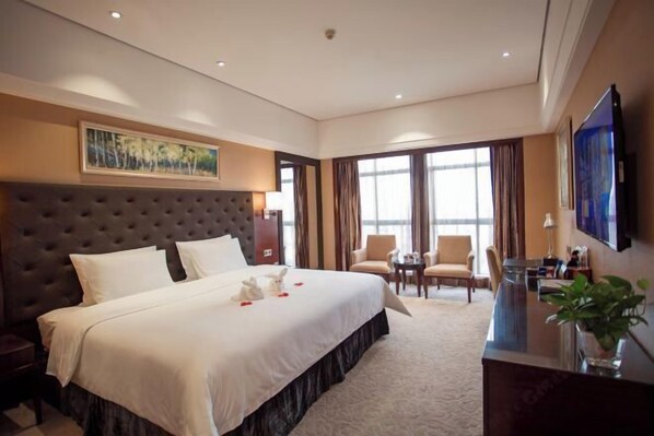 A hotel room with a large bed, a desk, two chairs, a TV, and a painting on the wall. - Jinlong Yufeng Hotel (Changde Huanlecheng High Speed Railway Station) (Changde)