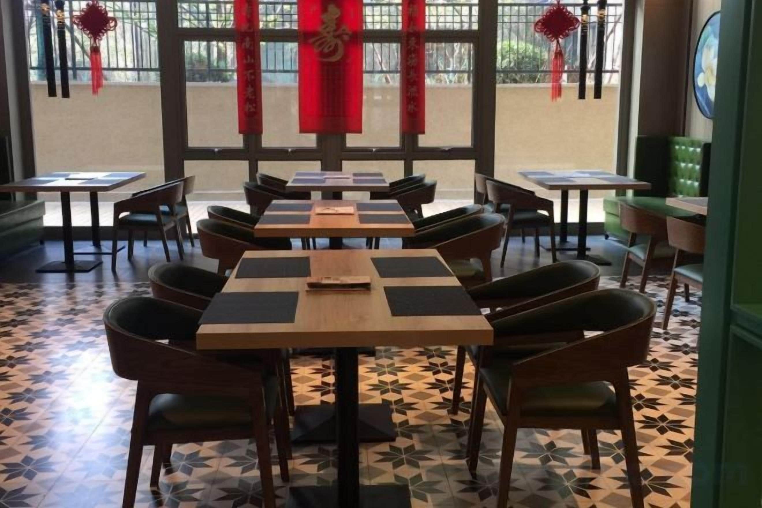 A restaurant with multiple tables and chairs, a patterned floor, and red decorations.