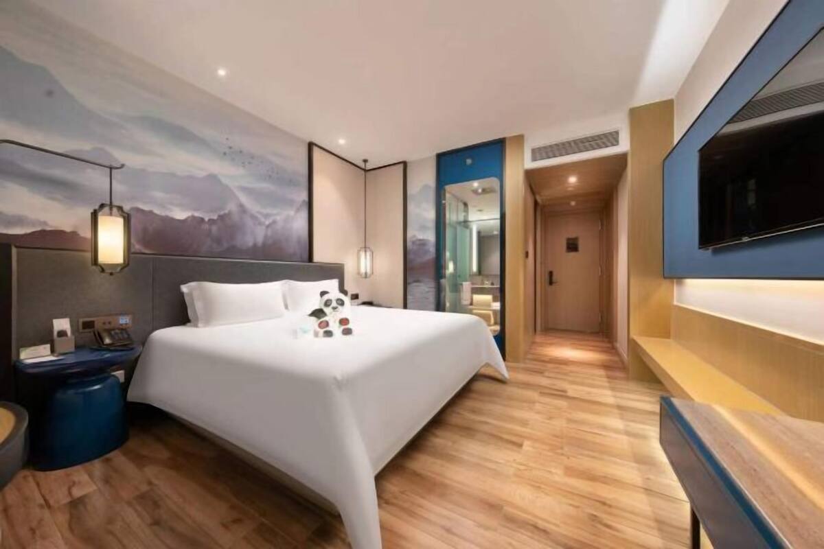 Una habitación de hotel moderna con cama, mesita de noche, lámpara y televisor montado en la pared.