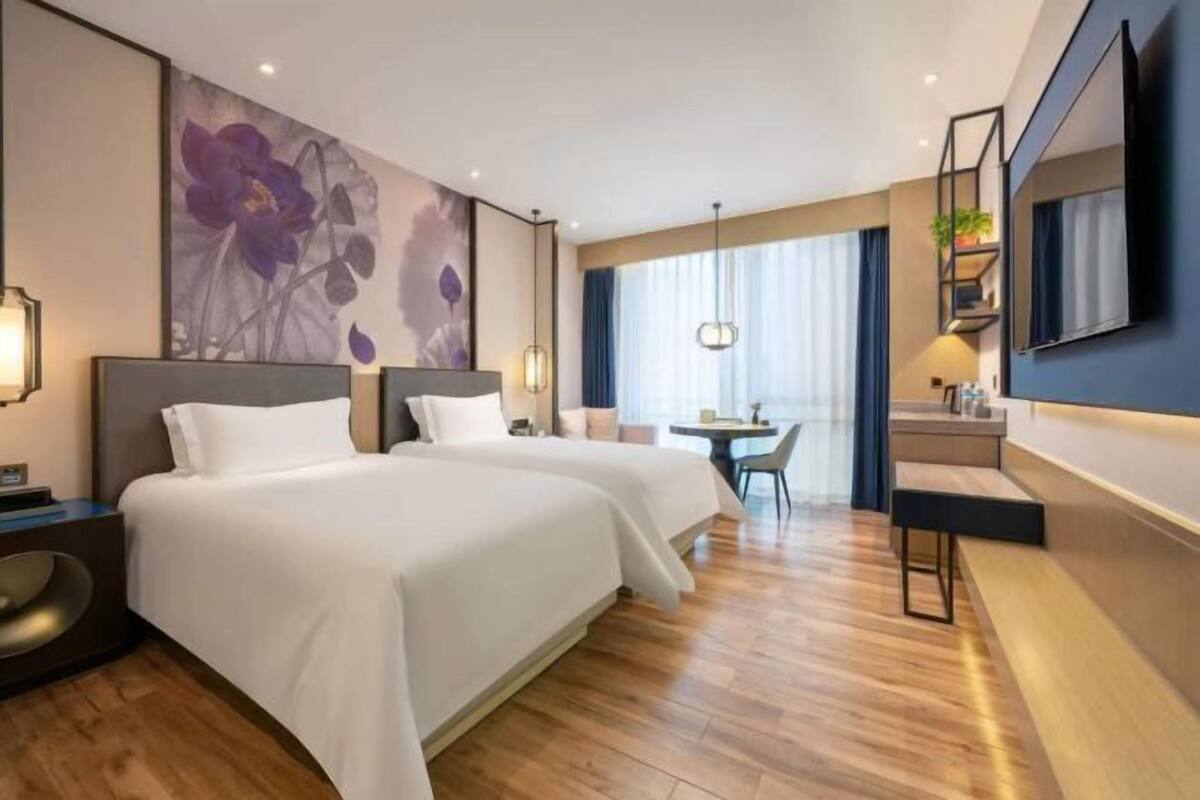 Habitación de hotel con dos camas, un escritorio, una silla, un televisor y un ventanal con cortinas.