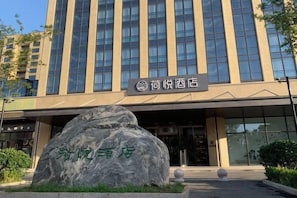A hotel with a large rock in the entrance area, a signboard above the entrance, and a modern building facade with vertical windows. - Heyue Hotel（Olympic Sports Center Store） (Jinan)