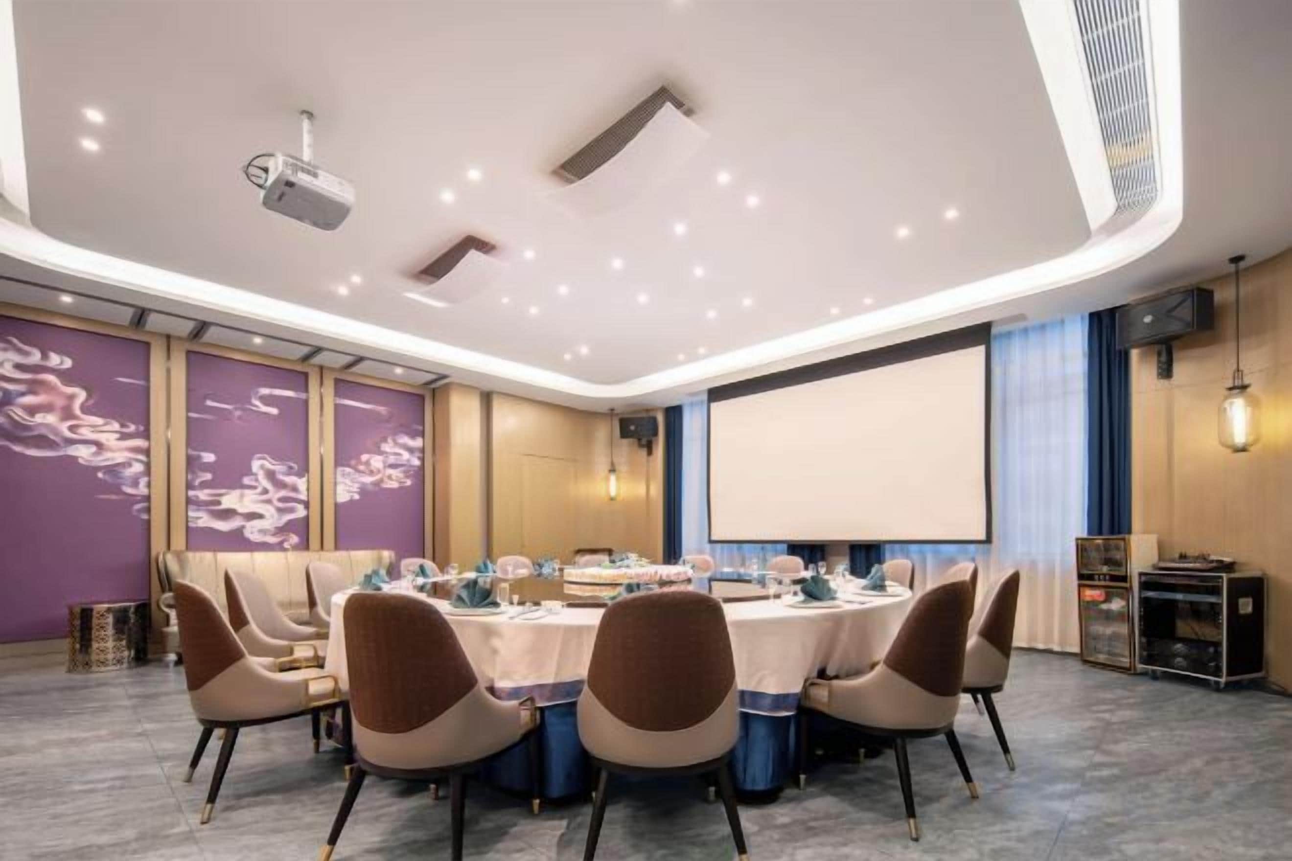 A conference room with a round table, chairs, a projector, and a screen.
