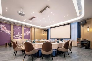 A conference room with a round table, chairs, a projector, and a screen. - Heyue Hotel（Olympic Sports Center Store） (Jinan)