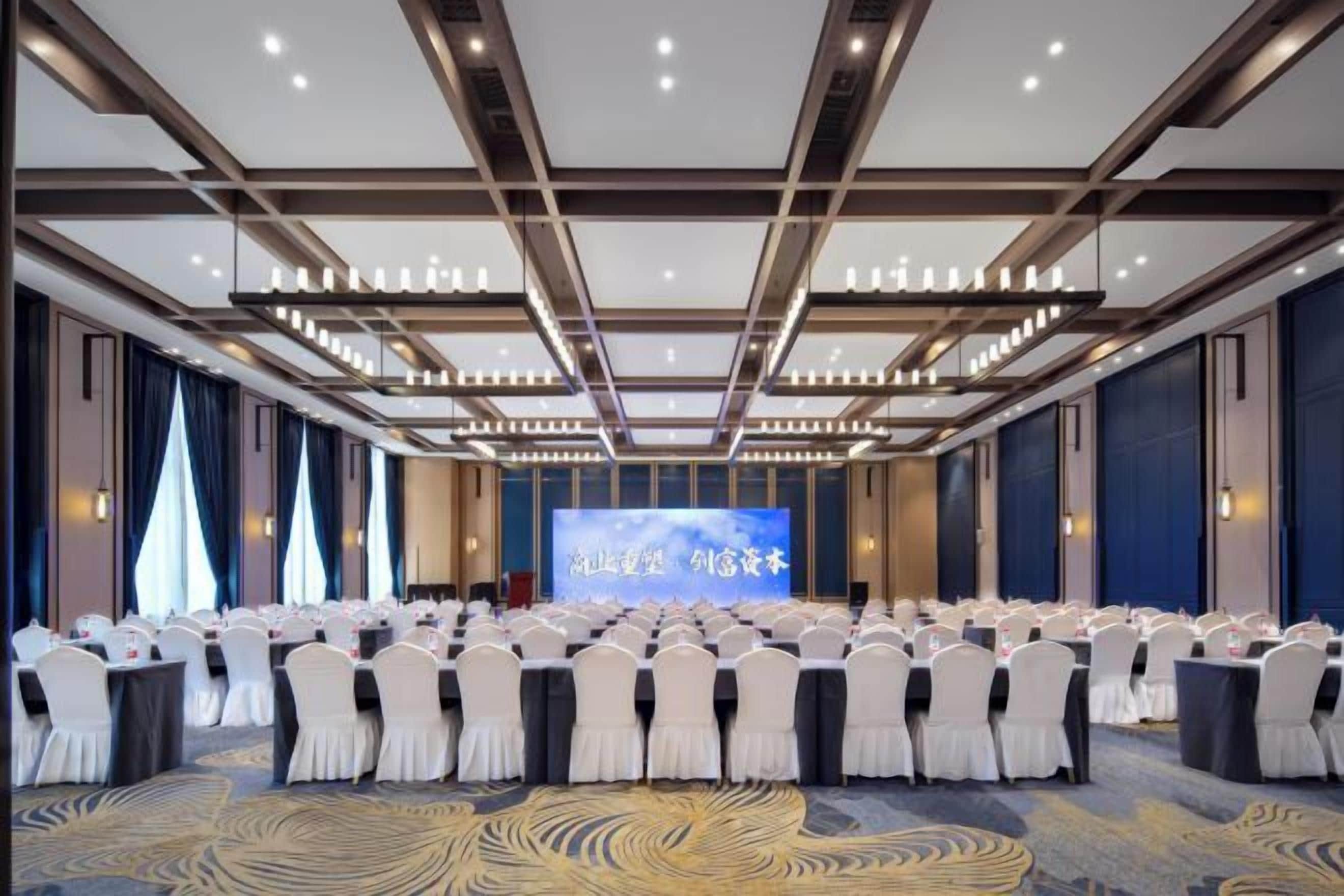 A conference room with rows of chairs, a stage with a screen, and a carpeted floor.