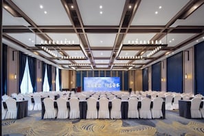 A conference room with rows of chairs, a stage with a screen, and a carpeted floor. - Heyue Hotel（Olympic Sports Center Store） (Jinan)