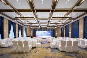 A conference room with round tables, white chairs, and a large screen at the front. - Heyue Hotel（Olympic Sports Center Store） (Jinan)