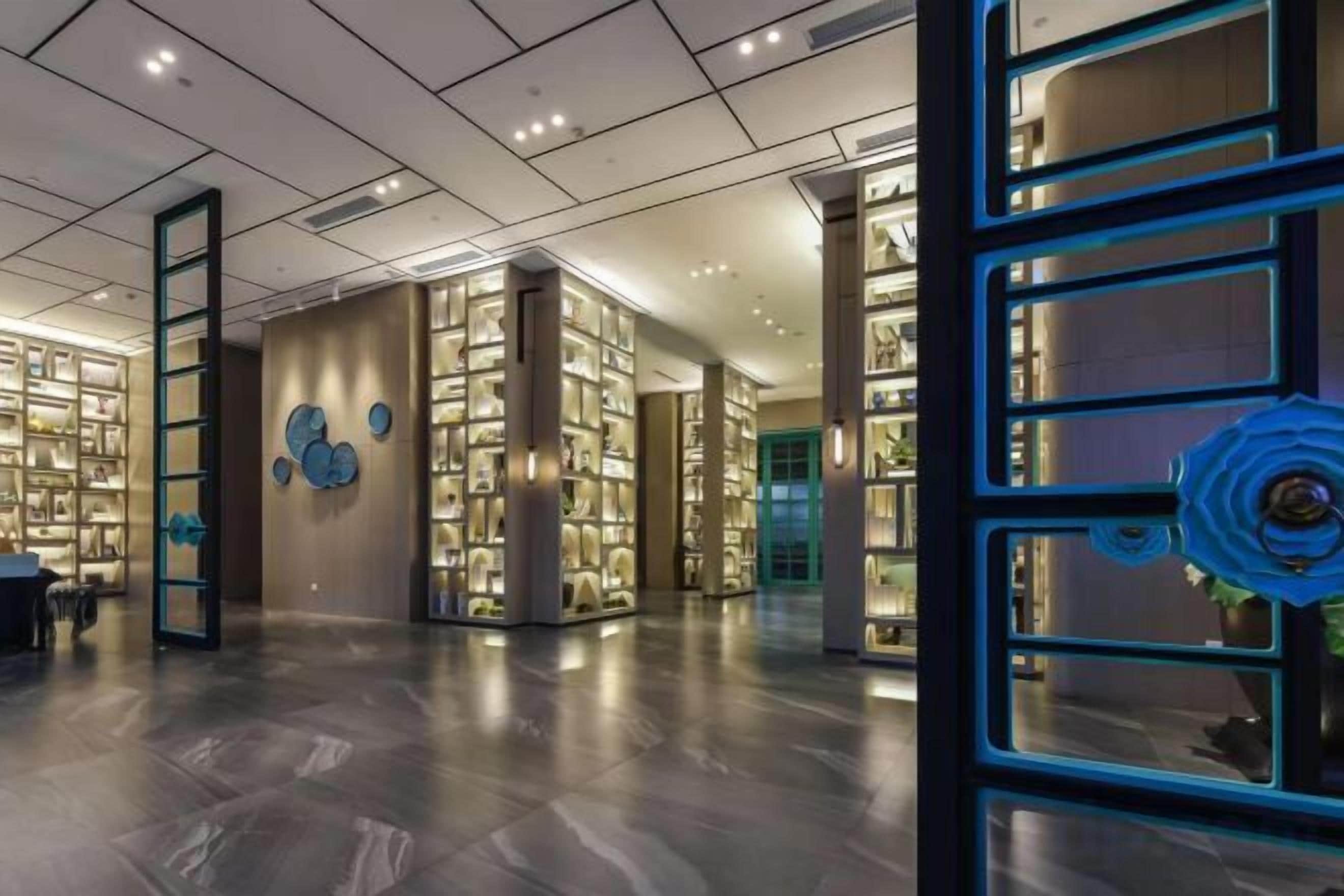 Um hall espaçoso com design moderno, apresentando uma área ampla e luminosa, piso lustroso, escadaria central e uma série de vitrines iluminadas.