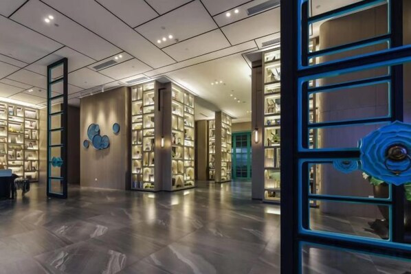 A spacious lobby with a modern design, featuring a large open area with a polished floor, a central staircase, and a series of illuminated display cases.