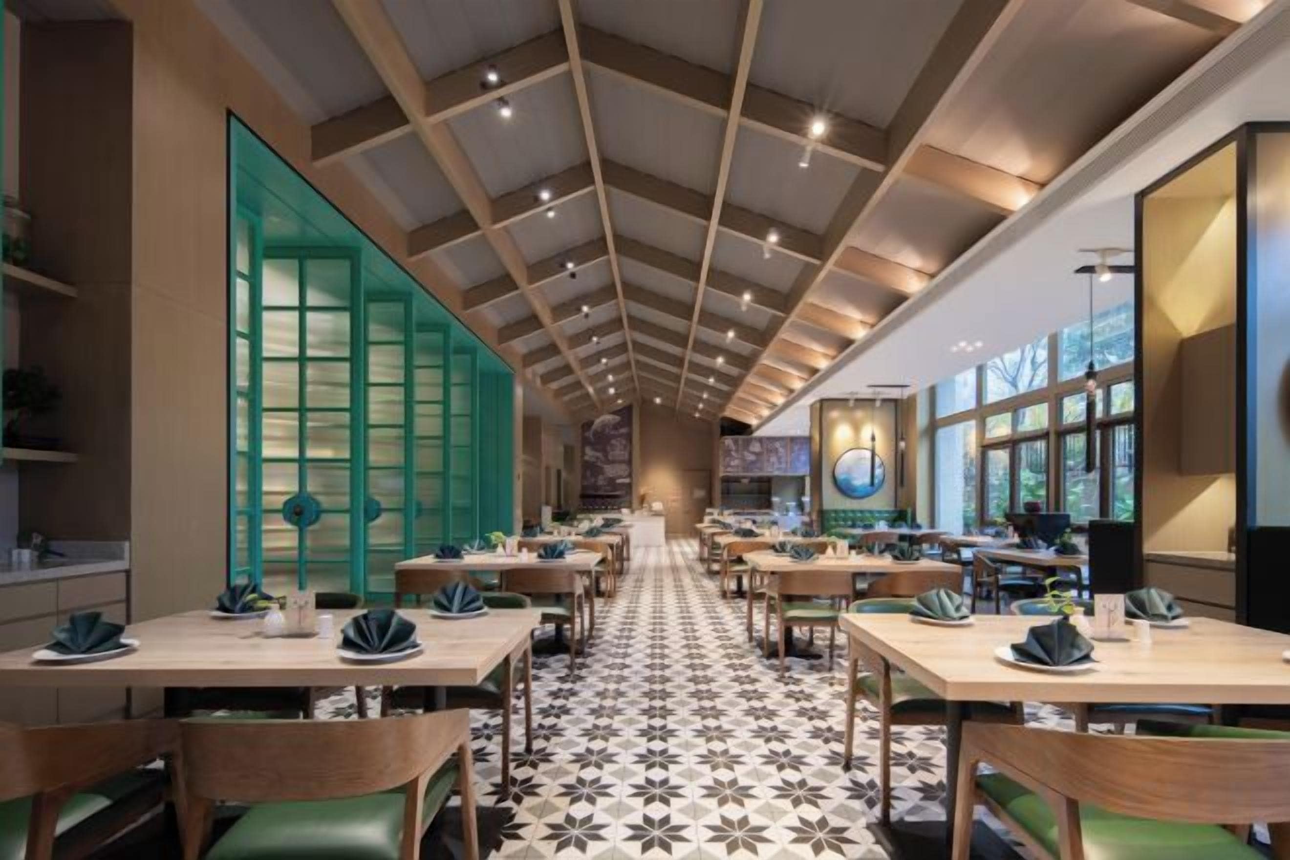 Interior de restaurante con una barra larga, sillas verdes y un suelo estampado.