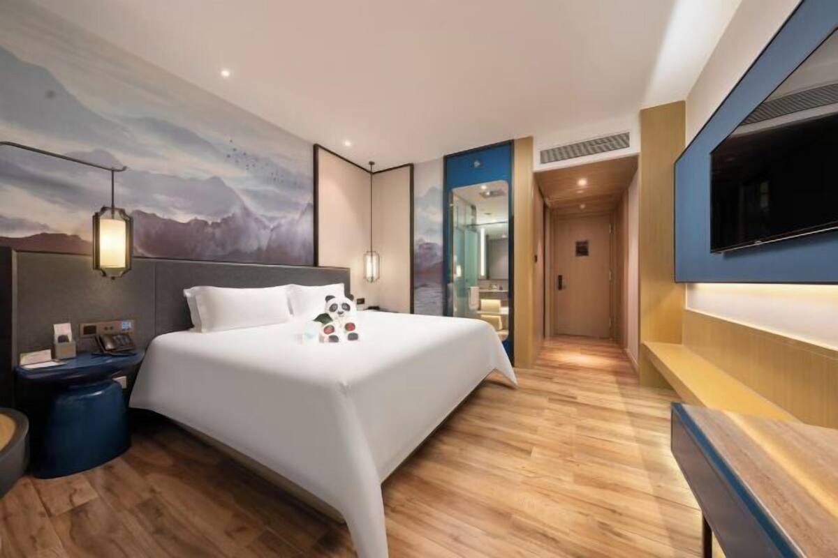 Una habitación de hotel moderna con una cama grande, un televisor de pantalla plana, una mesita de noche y un televisor instalado en la pared.