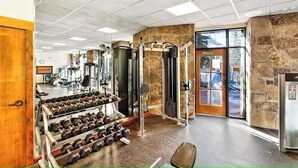 Un gimnasio con equipo de levantamiento de pesas, un soporte para mancuernas y una pared de piedra.