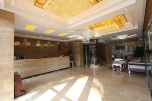 A hotel lobby with a reception desk, a marble column, and a chandelier.