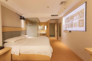 Una habitación de hotel con cama, mesita de noche, televisor montado en la pared y espejo.