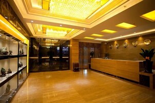 Un vestíbulo de hotel con una recepción, una puerta de cristal de acceso y suelo de madera.