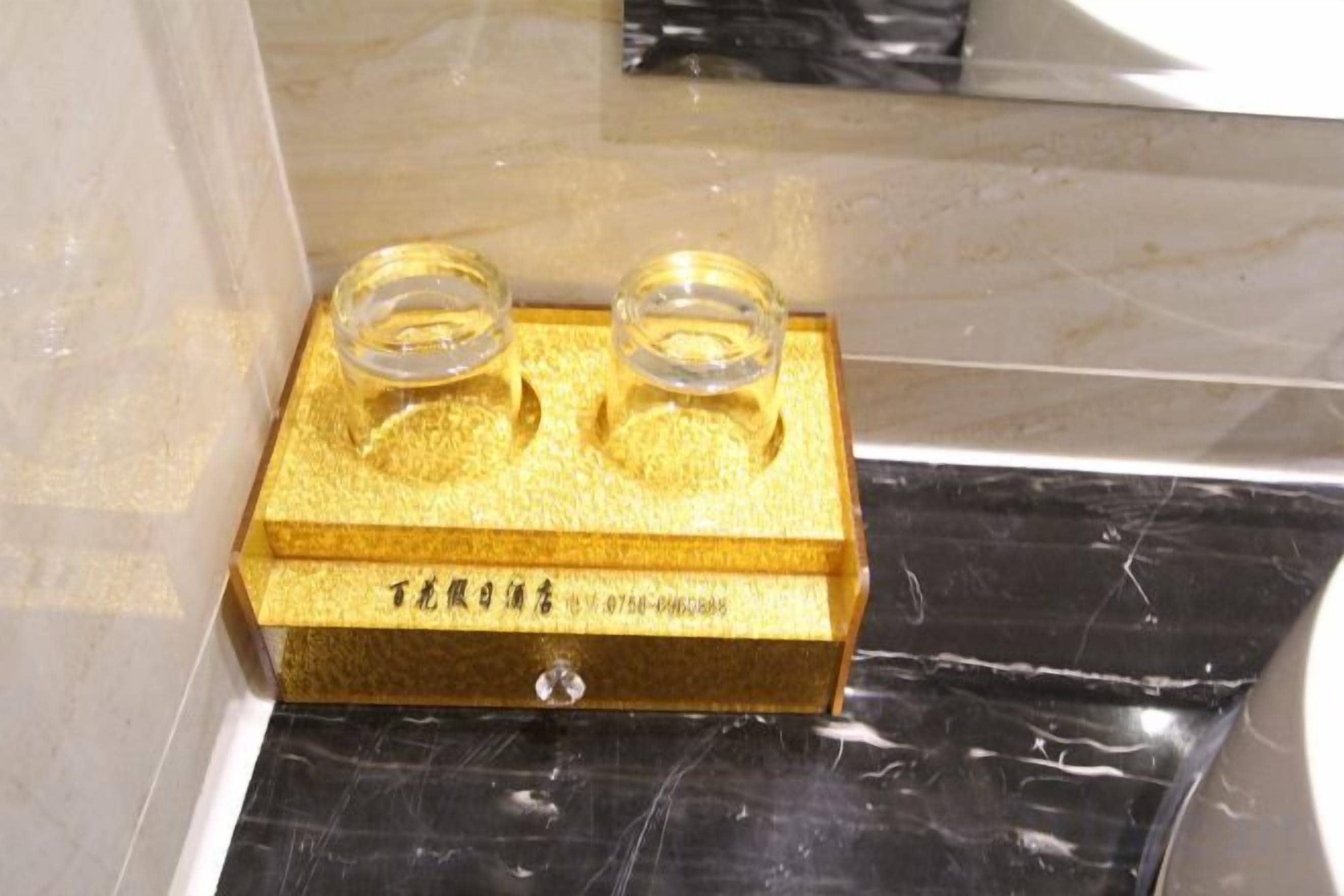 A gold-colored object with two clear glass containers on top, placed on a surface with a reflective black and white pattern.