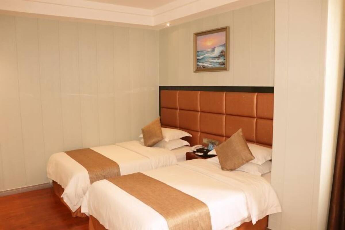 Ein Hotelzimmer mit zwei Betten, einem großen Gemälde, das einen Sonnenuntergang über dem Meer zeigt, und Holzboden.