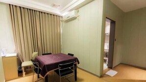 A room with a table, chairs, a small desk, a chair, a curtain, and a door. - Baihua Holiday Hotel (Guangning)