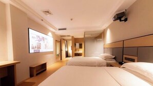 A hotel room with a large bed, a desk, a TV screen, and a mirror. - Baihua Holiday Hotel (Guangning)