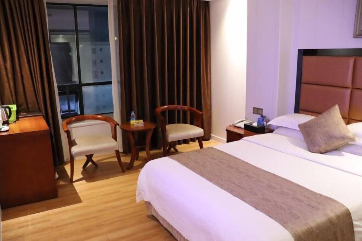 Ein Hotelzimmer mit Bett, Schreibtisch, Stuhl, Nachttisch und einem Fenster mit Vorhängen.
