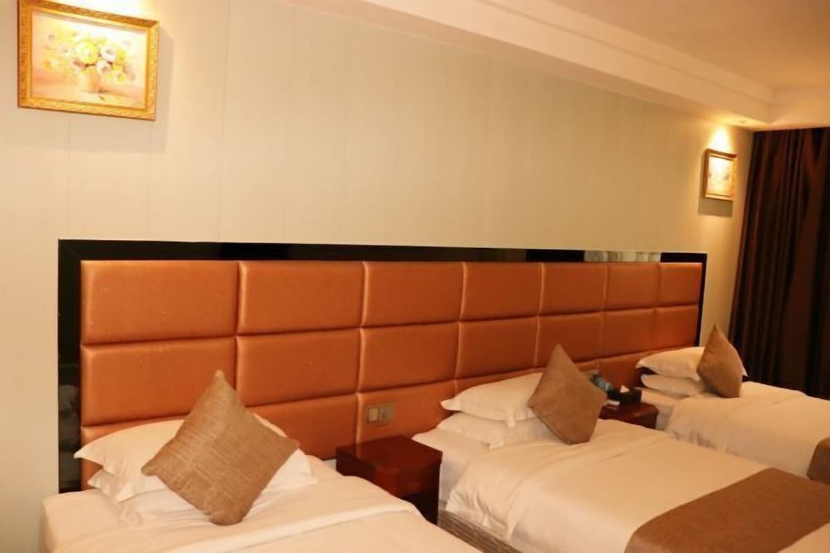 Een hotelkamer met een groot bed, een kleiner bed, een nachtkastje en een wandlamp.