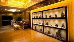 A lobby with a marble floor, a reception desk, a seating area with a sofa and chairs, and a wall display of sculptures. - Baihua Holiday Hotel (Guangning)