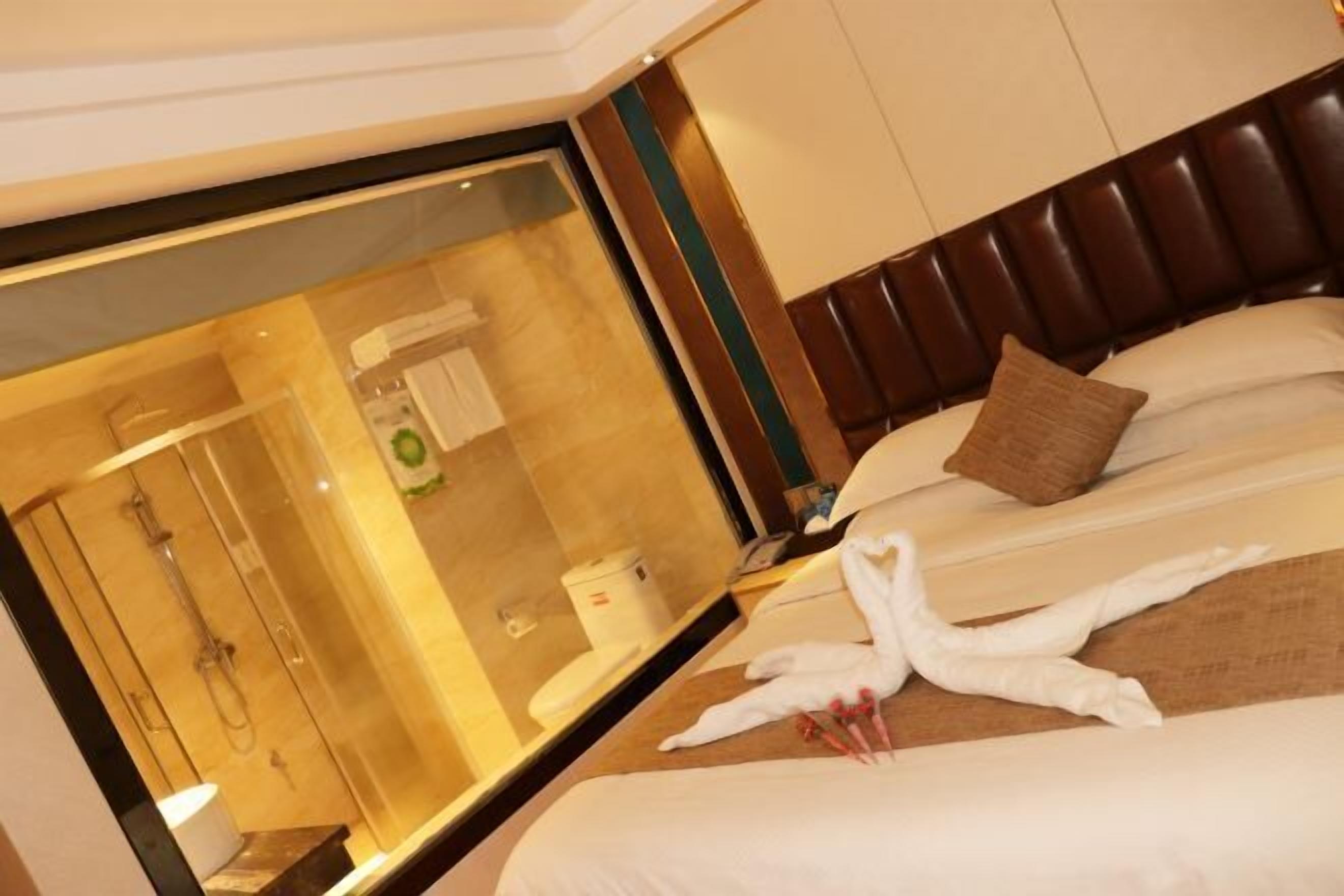 Habitación de hotel con un espejo grande, una cama con ropa de cama blanca, un cabecero marrón y una escultura de toallas.