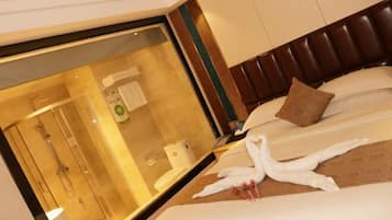 Habitación de hotel con un espejo grande, una cama con ropa de cama blanca, un cabecero marrón y una escultura de toallas.