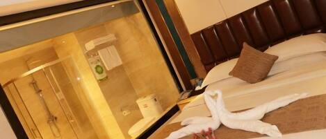 A hotel room with a large mirror, a bed with white linens, a brown headboard, and a towel art installation.