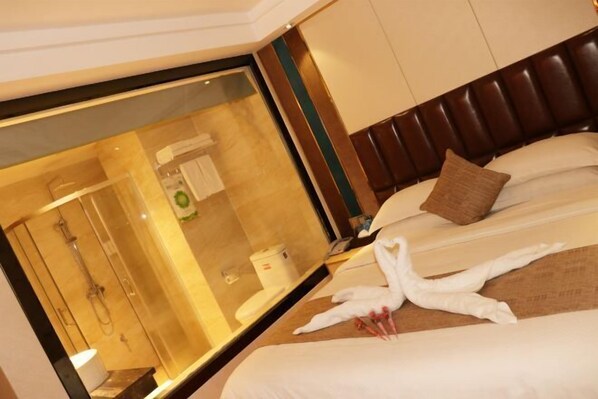 Hotelkamer met een grote spiegel, een bed met witte lakens, een bruin hoofdeinde en een handdoeksculptuur.